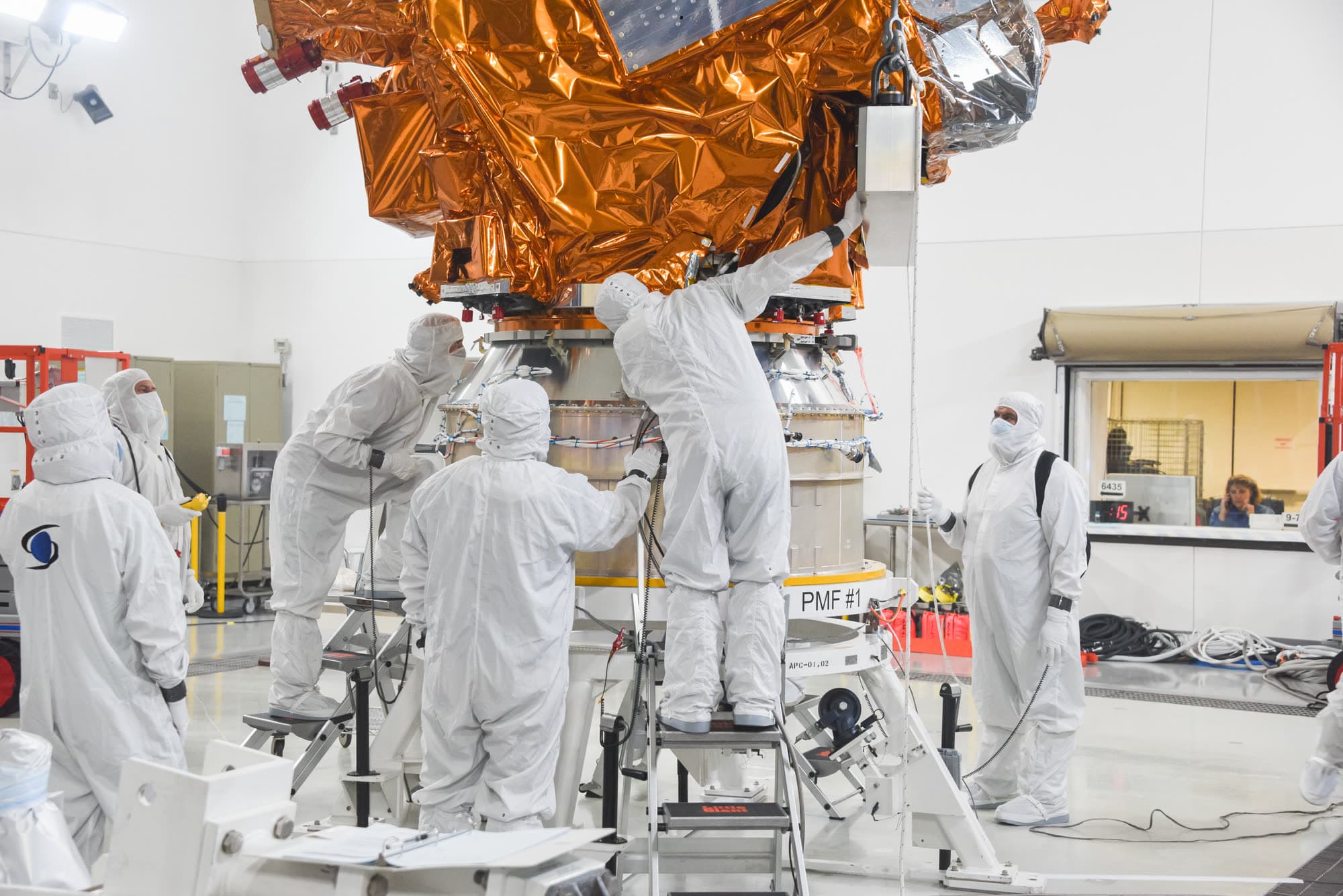 Technicians in white cleanroom suits prepare the JPSS-2 weather satellite inside a processing facility at Vandenberg